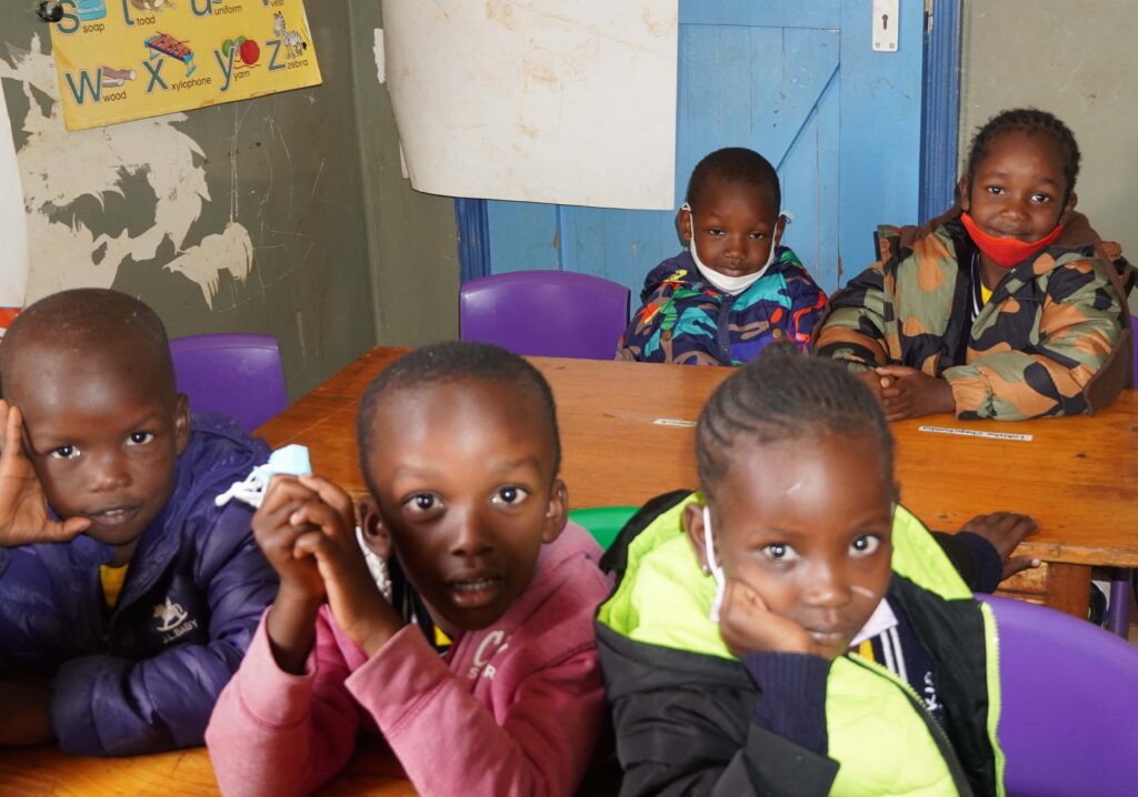 Young children in Africa sitting at classroom desks wearing jackets and face masks.
