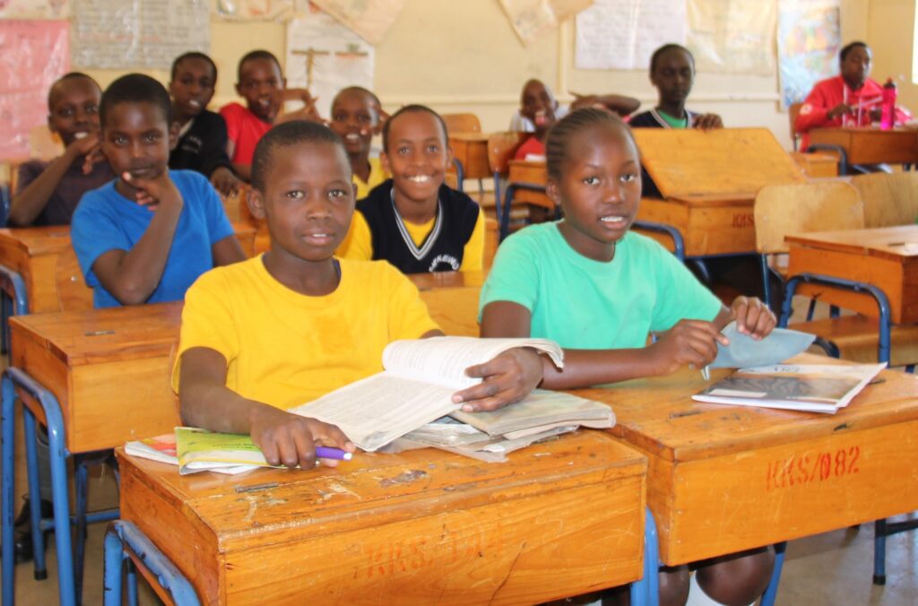 Students in Africa sitting at wooden desks and reading books in a classroom.