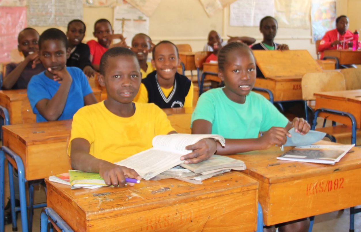Smiling students in a classroom with wooden desks and open books in Africa.