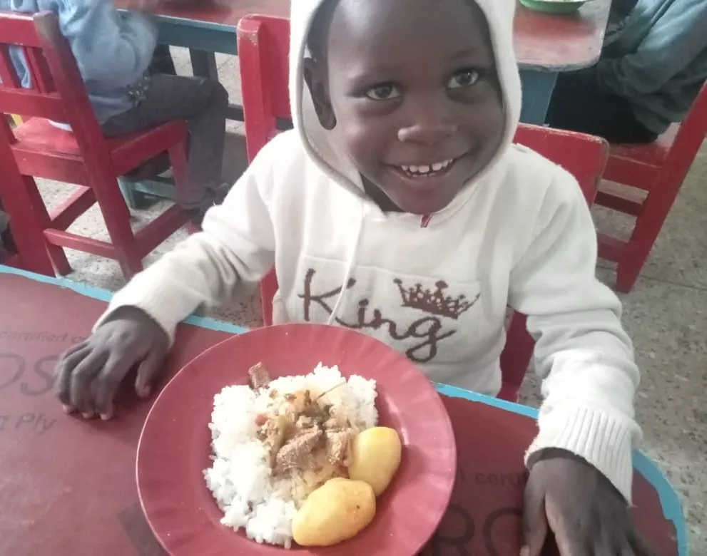 Smiling child with rice and potatoes at a school lunch table in Kenya.