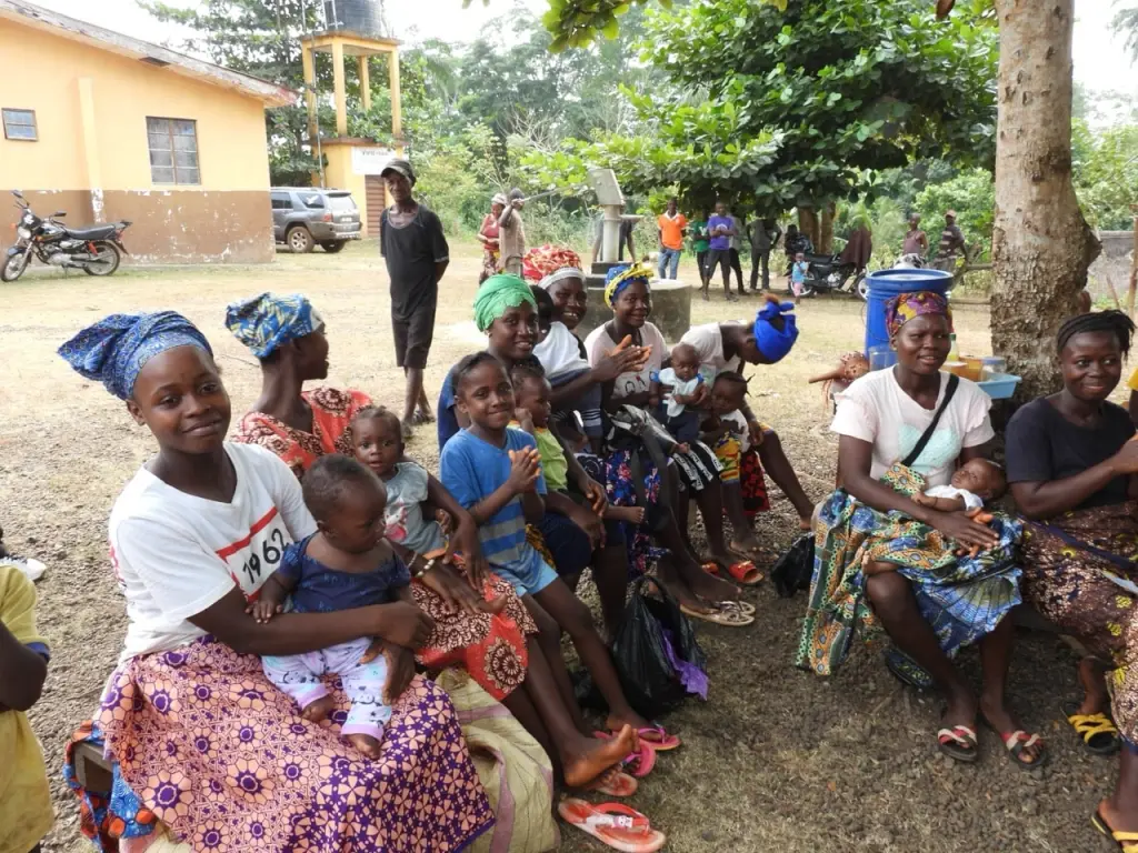 A community of African mothers and young children sitting together outdoors.