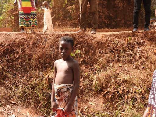 A young boy stands on a dirt embankment in rural Sierra Leone, looking directly at the camera.