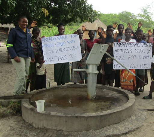 Grateful Zambian villagers hold thank you signs next to their new borehole, celebrating access to safe water.