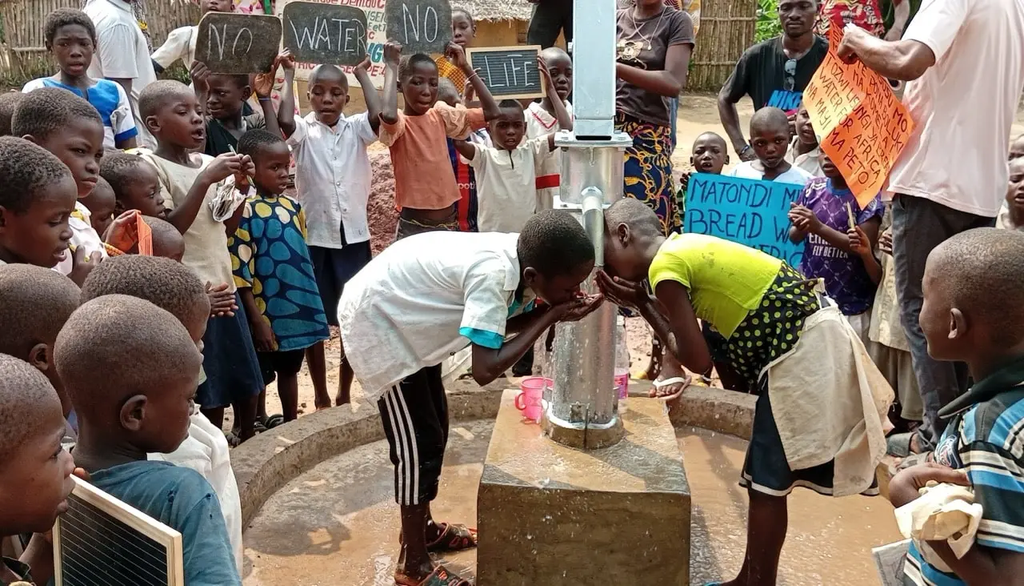 Congolese children joyfully drink from a new, life-saving water well in their village while others hold signs of gratitude.