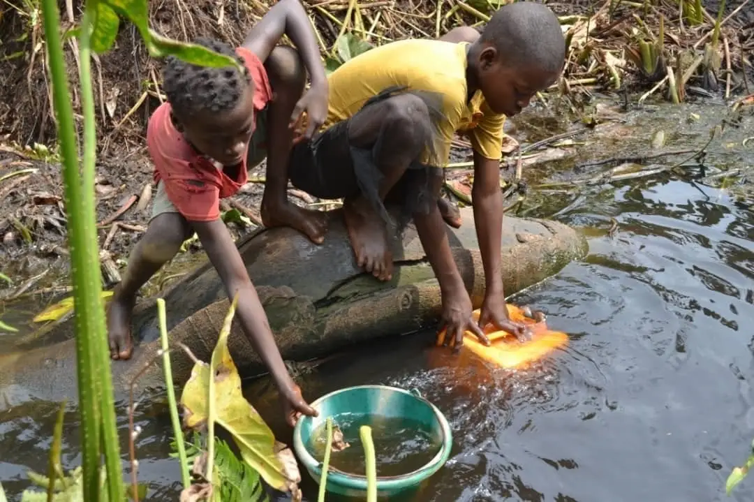 Two young Congolese boys are forced to collect unsafe drinking water from a murky, unprotected river.
