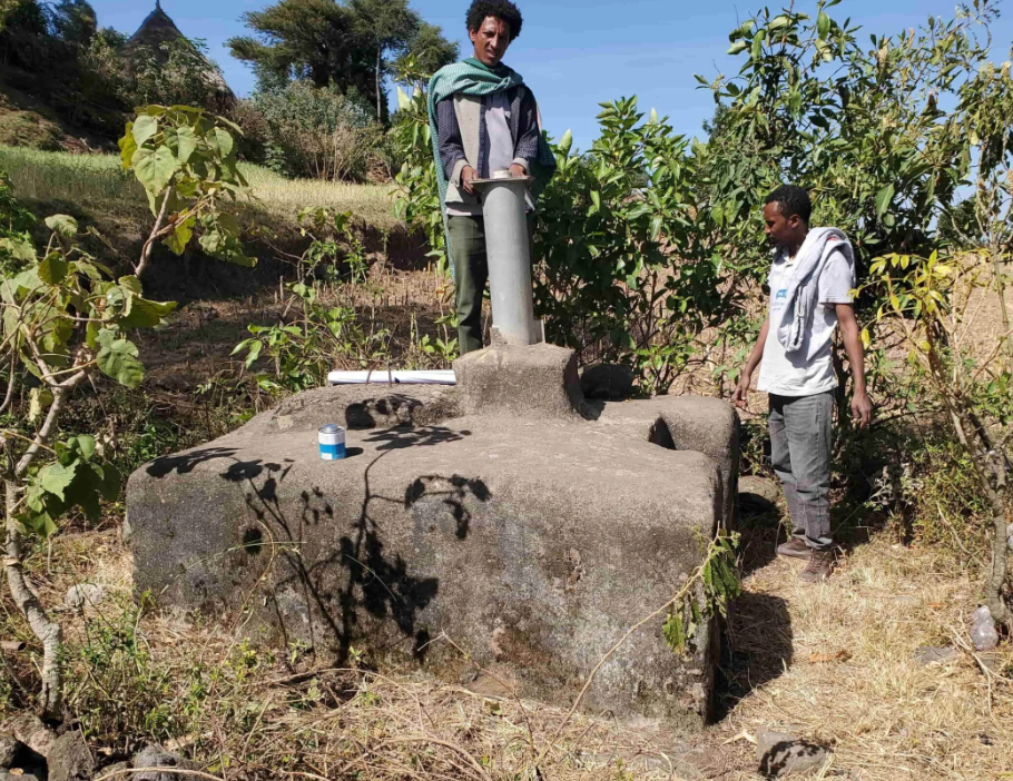 Two young Ethiopian men inspect and work on the repair of a concrete community water well in a rural area.