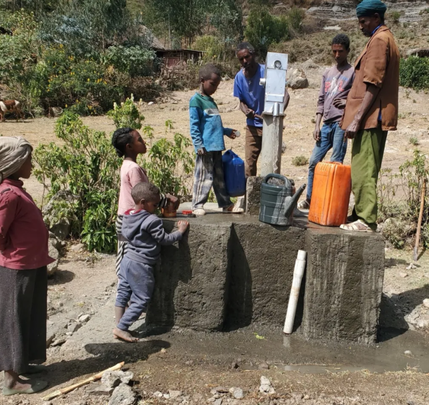 Ethiopian community members, including a young boy, pump clean water from a rural hand pump.
